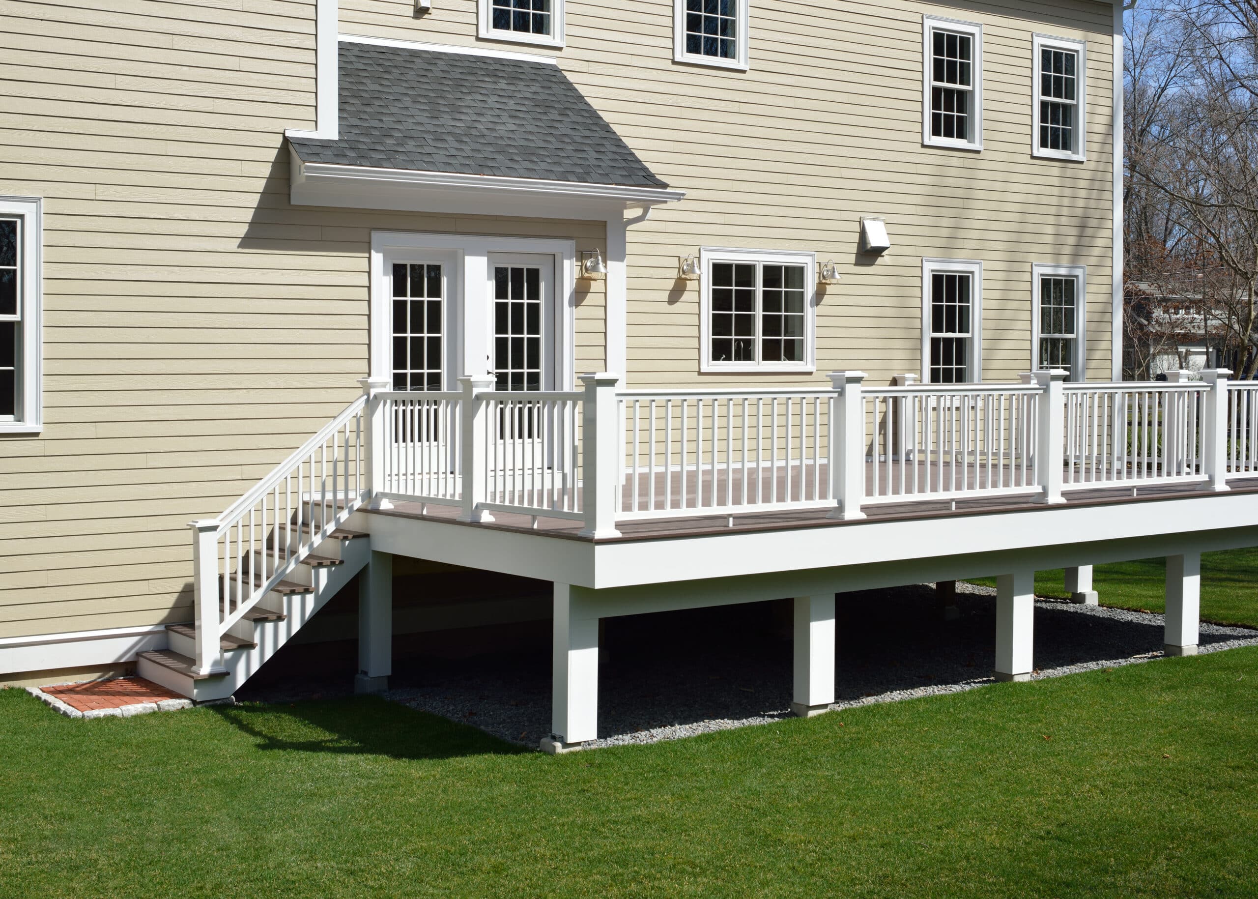 Elevated wooden deck with white railings attached to a beige house, featuring a staircase leading to a well-maintained green lawn.