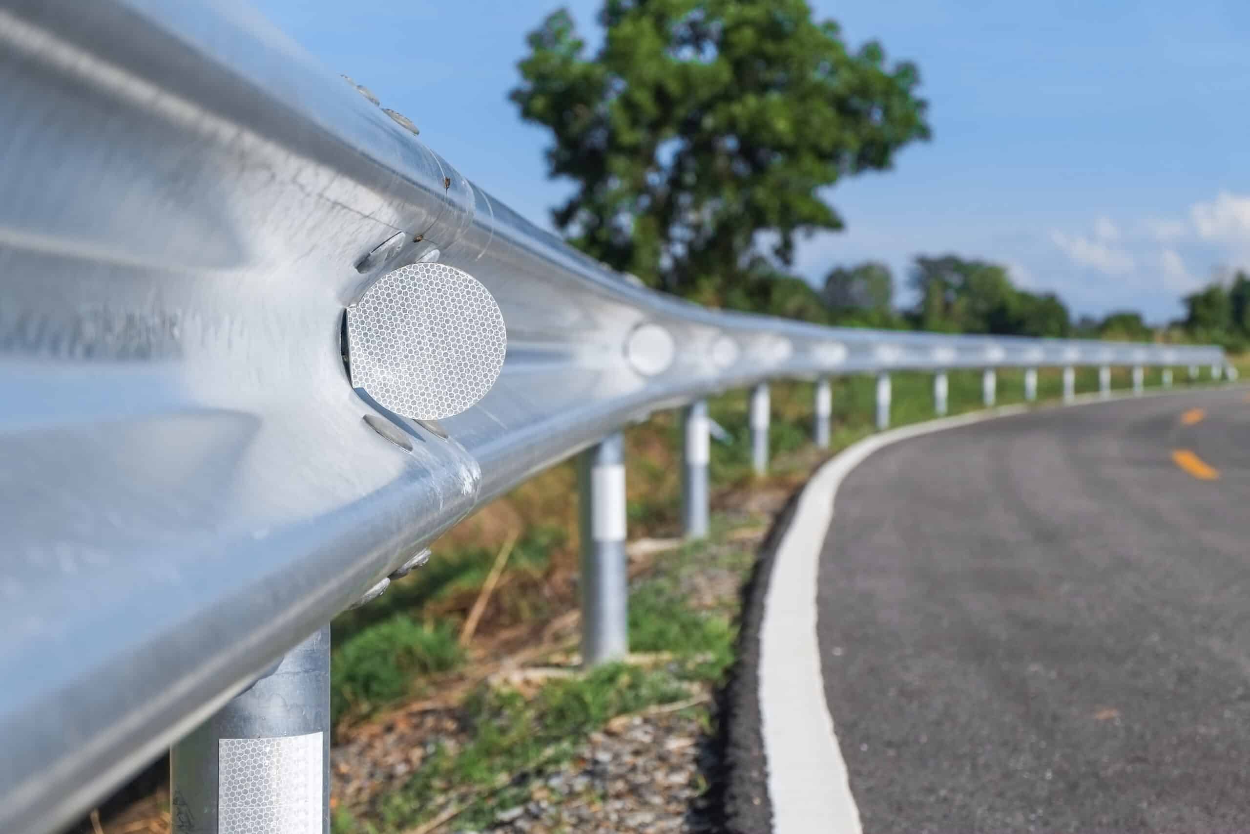 A sturdy metal highway guardrail with reflectors, installed along a curved road for enhanced safety by a railing installation near me service.