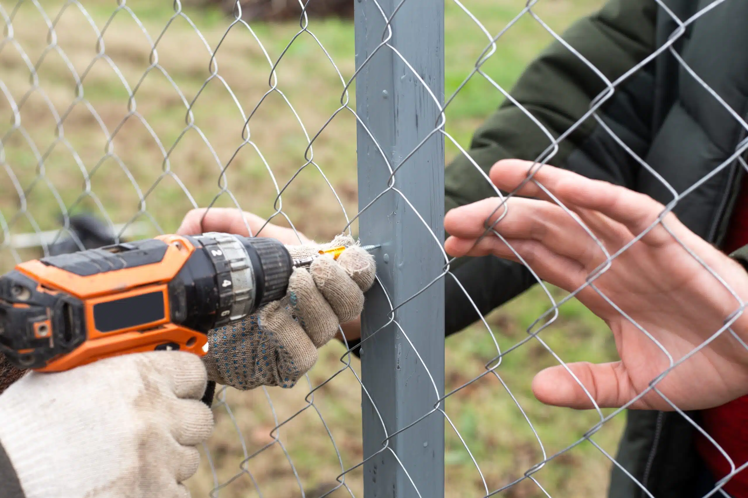 Two workers securing a chain-link fence with a power drill during a fence installation project in Philadelphia.