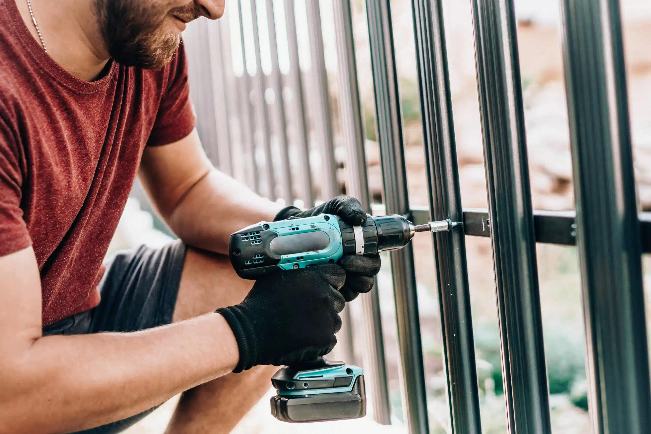A professional installer using a power drill to secure a black metal fence during a fence installation in Philadelphia.